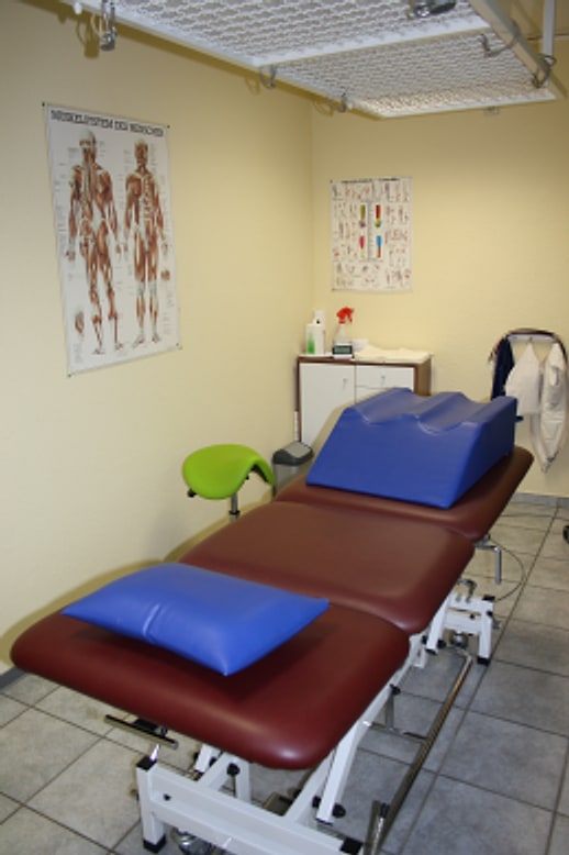 Behandlungsraum mit Therapieliege, anatomischen Postern und Rollhocker